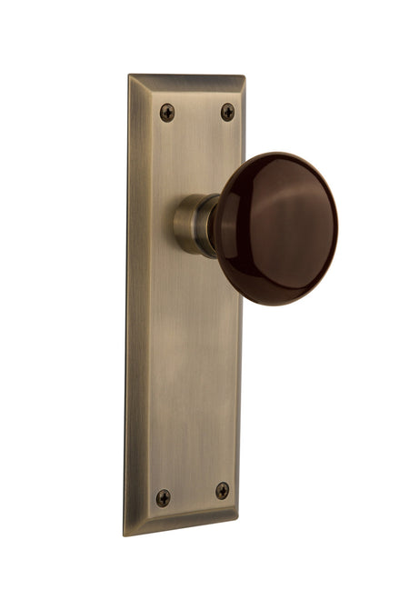 Nostalgic 710461: New York Backplate w/Brown Porcelain Knob Passage Door Set - Antique Brass