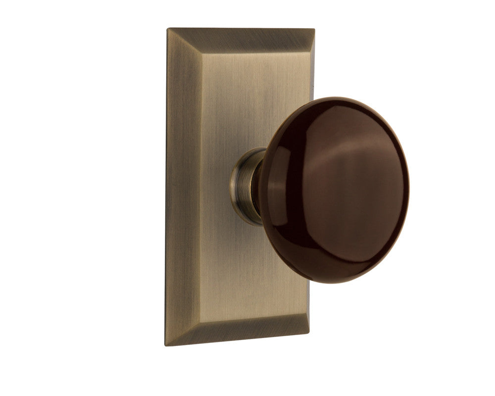 Nostalgic 713290: Studio Backplate w/Brown Porcelain Knob Passage Door Set - Antique Brass